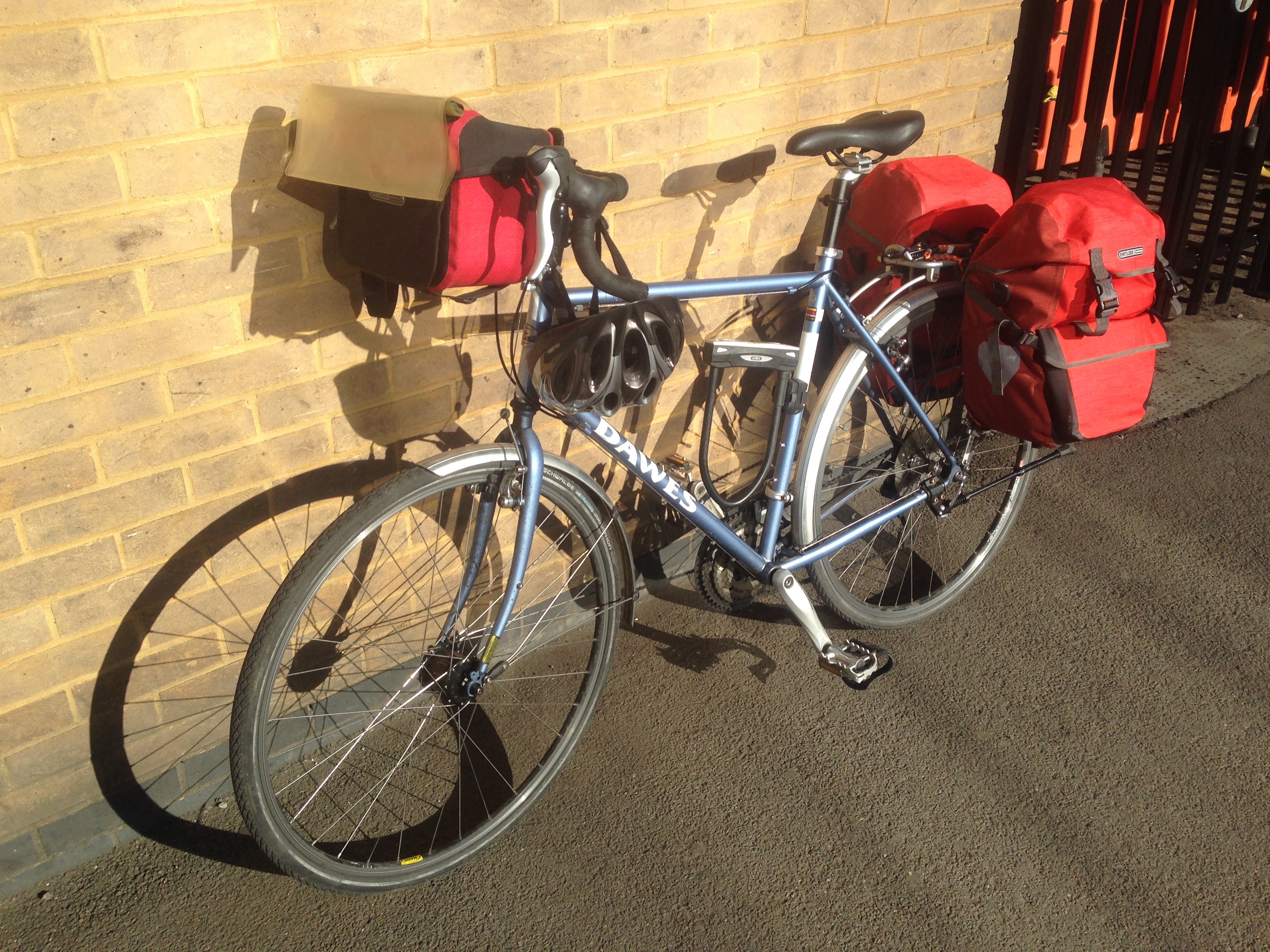 Photograph of a touring bicycle laden with panniers, leaning against a wall.